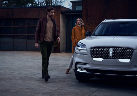 A man and a woman approaching a 2024 Lincoln Aviator® SUV, which illuminates certain lights when they are close | Caruso Lincoln in Long Beach CA