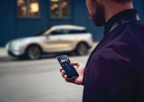 A person is shown interacting with a smartphone to connect to a Lincoln vehicle across the street. | Caruso Lincoln in Long Beach CA