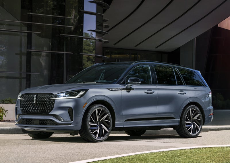 A gray 2025 Lincoln Aviator® SUV is parked outside a modern building showcasing the driver’s side of the vehicle. | Caruso Lincoln in Long Beach CA