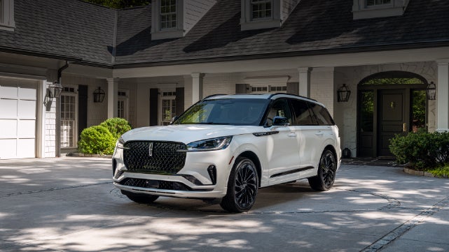 A white 2026 Lincoln Aviator® SUV is parked in the driveway of a luxury home. | Caruso Lincoln in Long Beach CA