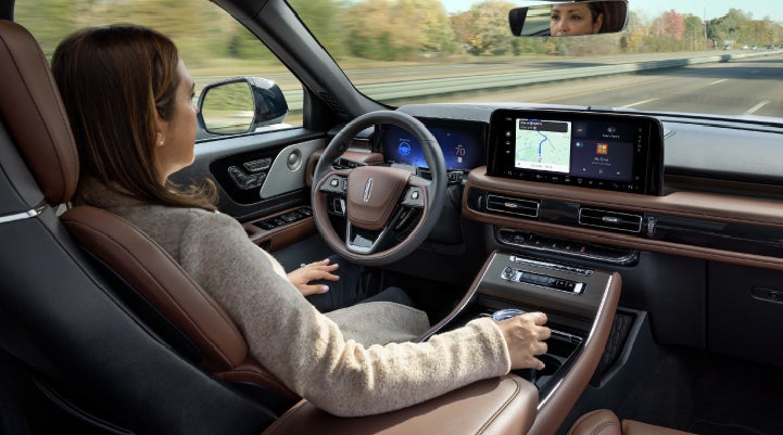 A 2027 Lincoln Aviator® SUV is being driven hands-free on a highway lined with trees. | Caruso Lincoln in Long Beach CA