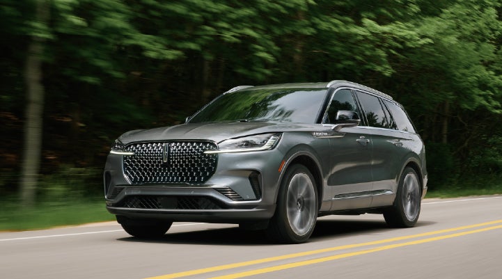 A 2027 Lincoln Aviator® SUV is being driven down a road lined with trees. | Caruso Lincoln in Long Beach CA